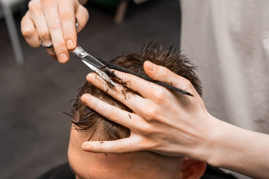 Barber uses scissors and comb to style the mans hair at the barbershop