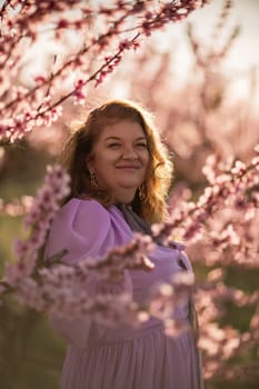 Woman blooming peach orchard. Against the backdrop of a picturesque peach orchard, a woman in a long pink dress and hat enjoys a peaceful walk in the park, surrounded by the beauty of nature