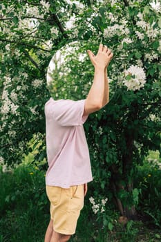 Creative male portrait with mirror in a blooming apples spring garden