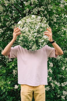 Creative male portrait with mirror in a blooming apples spring garden