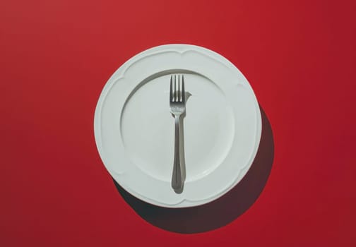 Empty plate with fork and knife on red background, table setting for corporate event or medical conference