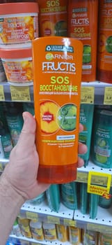 Bobruisk, Belarus - May 1, 2024: A person holds a bottle of Garnier Fructis SOS Restoration Balm in the shampoo aisle of a grocery store, showcasing the product.