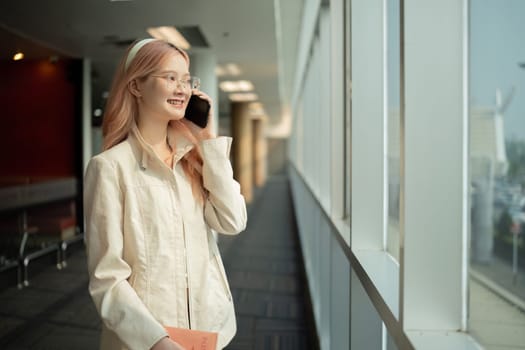 Asian woman talking on smartphone in airport terminal. Concept of travel, communication, and anticipation.