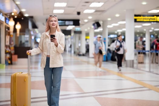 Young traveler with smartphone and luggage at airport terminal. Concept of modern travel, anticipation, and navigation.