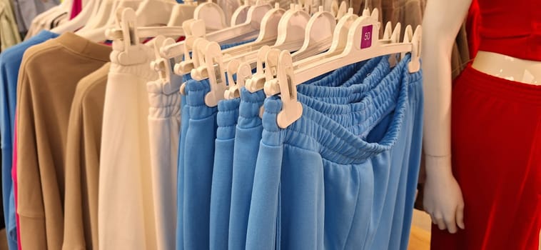 A retail store features a neatly organized clothing rack displaying blue pants among other garments during daytime shopping hours.