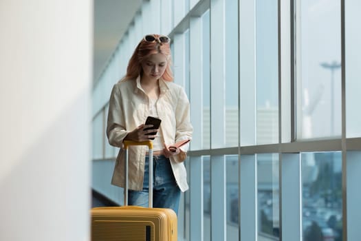 Asian woman talking on smartphone with luggage in airport terminal. Concept of travel, communication, and anticipation.