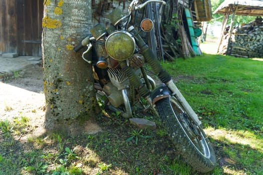 Kretinga, Lithuania - August 12, 2023: A motorcycle Jawa stands parked next to a tree in a grassy yard under the sun.