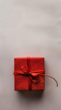 A vibrant red gift box with a satin ribbon lies on a textured white surface, evoking feelings of anticipation and celebration