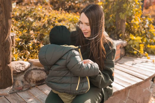Mother with her little son in autumn park. Woman zips up child jacket concept