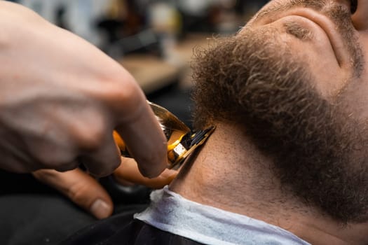 Barber swiftly cuts the clients beard with an automatic trimmer in the barbershop