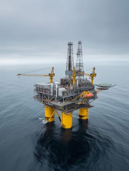 An offshore oil platform stands in stark contrast to the calm sea, with waves gently breaking in the foreground under an overcast sky