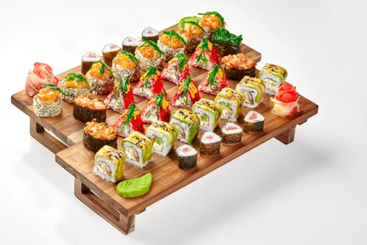 Enticing set of assorted Japanese sushi rolls and gunkan maki with avocado, tobiko, salmon, tuna and hiyashi wakame traditionally served with spicy wasabi and pickled ginger on wooden tray on white