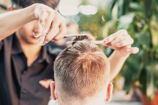 Neat young Vietnamese hairdresser makes haircut to male. Back view. Professional skills.