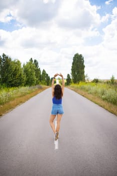 Attractive girl, stands posing, hands up in the middle of an asphalt road near the field, copies space for content