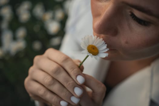 A woman is smelling a flower. The flower is white and yellow