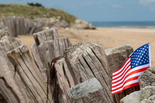 Utah Beach WWII with Flag of USA selective focus on flag. Sandy beach and fence posts. Normandy France rememberance of Veterans Day. High quality photo