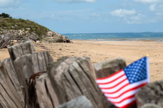 Utah Beach WWII with Flag of USA selective focus on beach and ocean. Sandy beach and fence posts. Normandy France rememberance of Veterans Day. High quality photo