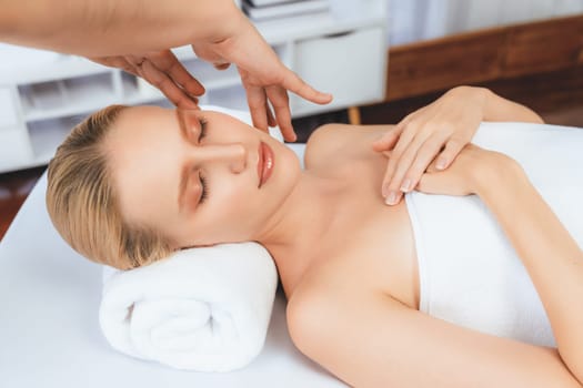 Caucasian woman enjoying relaxing anti-stress head massage and pampering facial beauty skin recreation leisure in dayspa modern light ambient at luxury resort or hotel spa salon. Quiescent