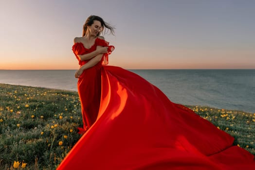 woman red dress standing grassy hillside. The sun is setting in the background, casting a warm glow over the scene. The woman is enjoying the beautiful view and the peaceful atmosphere