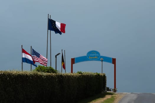 05 May 2023 Private Paradis Camp sign costal area of Utah beach. French, European Union, and USA and French Revolutionary flag are waving. Green blue cloudy sky. High quality photo