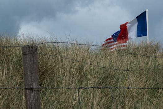 Normandy area of Utah beach. French, and USA and French Revolutionary flag are waving. Cloudy sky. High quality photo