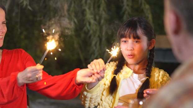 Girl hold sparkler in holiday celebration party under old senior couple eye. Adorable family enjoy play spark together. Multigeneration concept cross generation gap strengthen family bond. Divergence.