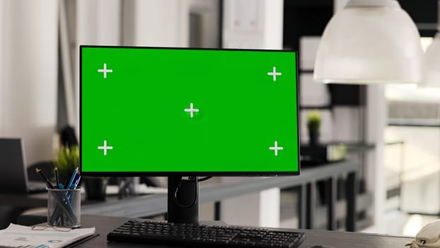 Empty workstation with computer running greenscreen on monitor, showing blank chromakey template in coworking space. Desk in open floor plan office with pc and isolated copyspace display.