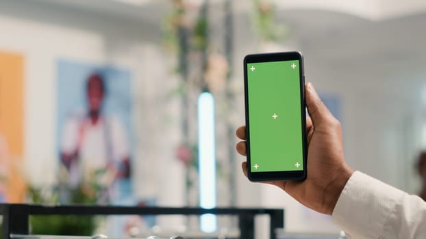 Close up shot of client holding green screen smartphone in premium clothing store, looking at online products. Customer with green screen mobile phone in fashion boutique doing internet shopping