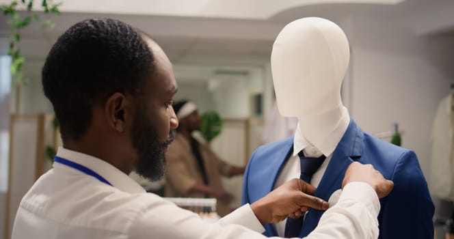 Employee working in clothing store during promotional season, arranging necktie on mannequin blazer. Shopkeeper placing pocket square on older collection garment on sale in fashion boutique