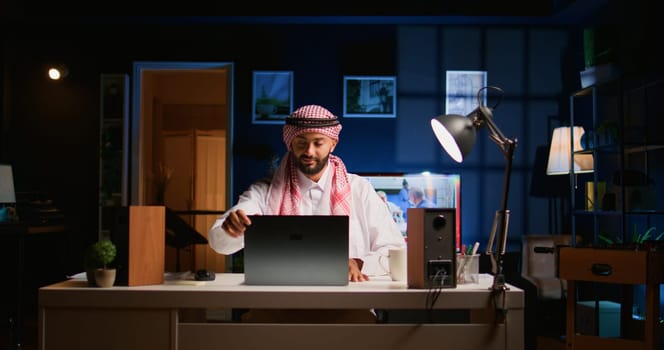 Arab employee arriving in stylish apartment personal office, starting important job tasks. Focused muslim teleworker typing on laptop keyboard, beginning work shift at home