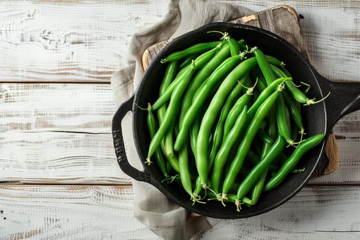 A metal bowl filled with fresh green beans sits on top of a wooden table.