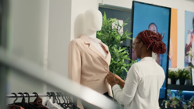 Woman working in second hand clothing shop arranging nice stylish blazer on mannequin to lure in clients. Storekeeper closing down buttons on formal garment in discount fashion store