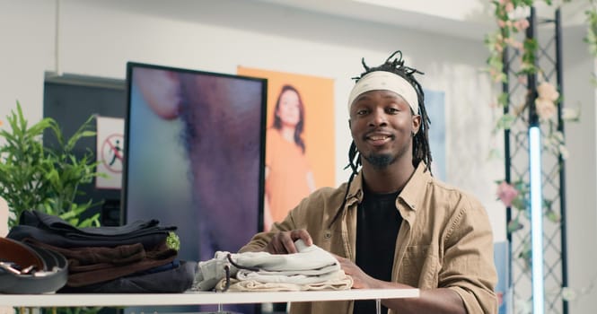 Portrait of smiling client buying stylish formal clothes on hanger in empty fancy fashion boutique. Cheerful BIPOC customer looking at exquisite designer clothing men collection in premium showroom