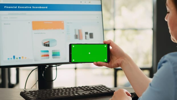 Businesswoman analyzing smartphone app with greenscreen template in startup coworking space. Person looking at isolated chromakey display with mockup on digital mobile device, copyspace.