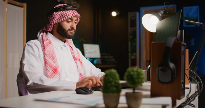 Muslim broker investor employee wearing islamic kandora in office checking stock exchange valuation financial profit numbers. Arab stockholder looking at market shares growth, handheld camera shot