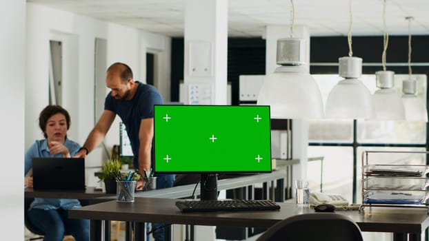 Workstation displaying greenscreen layout with copyspace on monitor at empty desk in urban coworking space. Chromakey display equipment adopted in smaller company operations. Tripod shot.