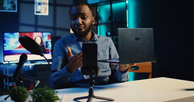 Media star films tech review of newly launched laptop, unboxing it and presenting specs to audience. Influencer showing notebook to fans, offering feedback of its performance, handheld camera shot