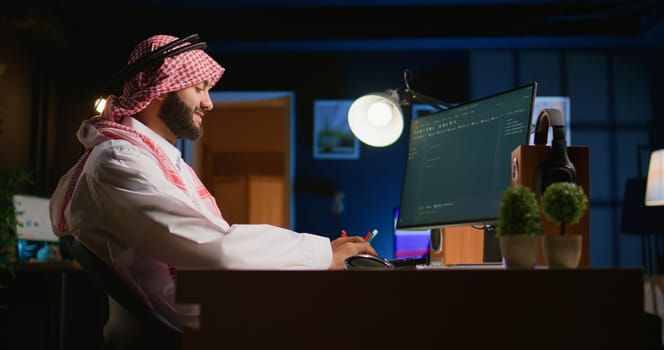 Smiling muslim engineer writing script code on computer screen using Java programming languages. Self employed Middle Eastern developer at home working on fixing database errors