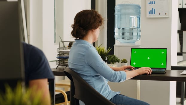 Office worker checks greenscreen on laptop, working in small business agency. Woman looking at screen showing isolated mockup template with chromakey copyspace, coworking space.