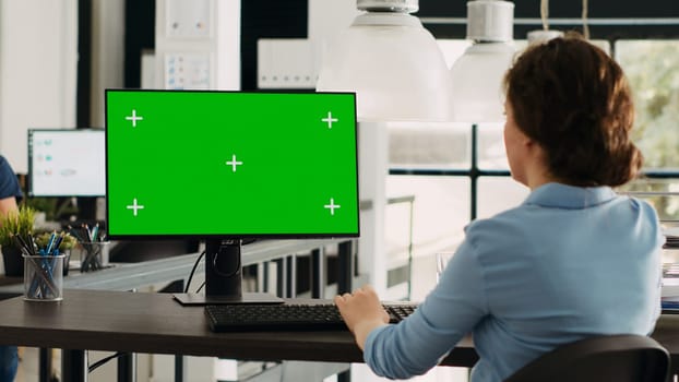 Manager working with isolated greenscreen on computer at workstation, looking at chromakey display with mockup template on desk. Businesswoman using pc in coworking space.