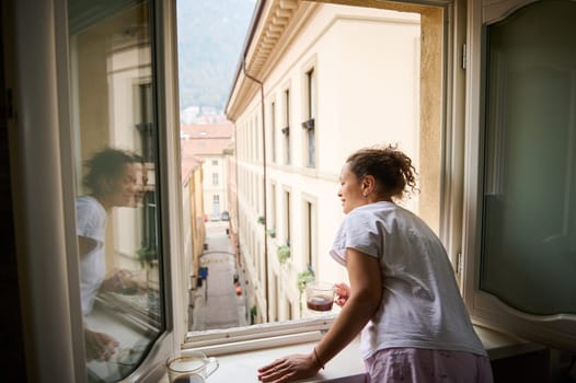 Cheerful happy woman tourist, looking through the window, enjoying the beautiful view of medieval city of Como in Italy. People. Lifestyle. Travel and tourism. Leisure activity