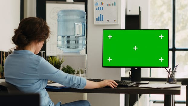 Businesswoman working at computer running isolated mockup display, sitting at office desk during work program. Employee using modern monitor with greenscreen copyspace layout at job.