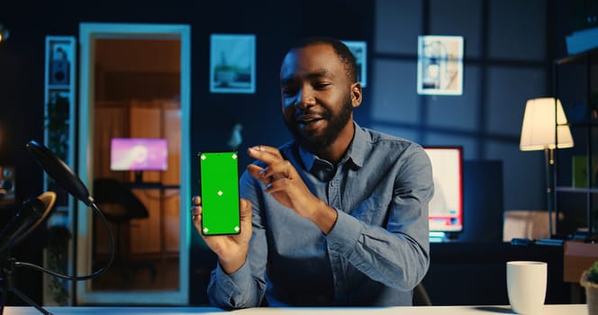 Content creator holding green screen product, being sponsored by tech brand to film unboxing review. BIPOC Influencer showing isolated screen phone recommendation to viewers