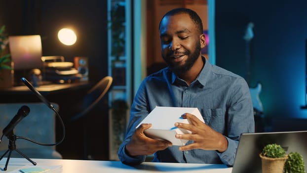 BIPOC tech content creator filming technology review of newly released smartphone, unboxing it and presenting parameters to audience. Internet star showing phone to subscribers