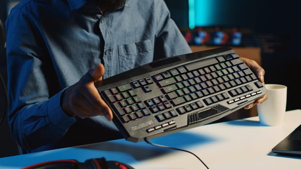 African american content creator in dimly lit living room uses camera to film RGB lights keyboard review for online streaming platforms. Media star hosts internet show, unboxing peripherals, close up