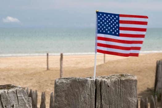 Utah Beach in Normandy, France. Closeup USA flag on wood sea fence. Grass and sand dunes. Sunny sky light ble clouds. High quality photo