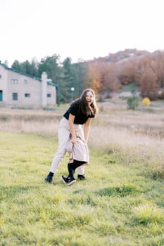 Laughing mother hugs little girl cuddled on her lap on green lawn. High quality photo