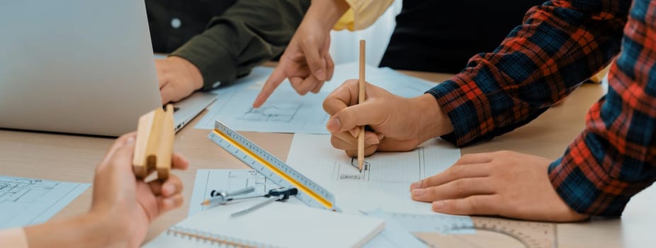 Professional architect team discussion about architectural project on meeting table with blueprint and wooden block scatter around at modern office. Closeup. Focus on hand. Delineation.