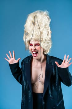 Bizarre screaming princess, dressed as queen in jacket and vintage royal wig with red makeup, isolated on blue background. Concept of comparing eras, modernity, renaissance, and beauty.