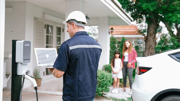 Qualified technician working on home EV charging station installation, making troubleshooting and configuration setup on charging system with empty laptop screem for EV at home. Synchronos